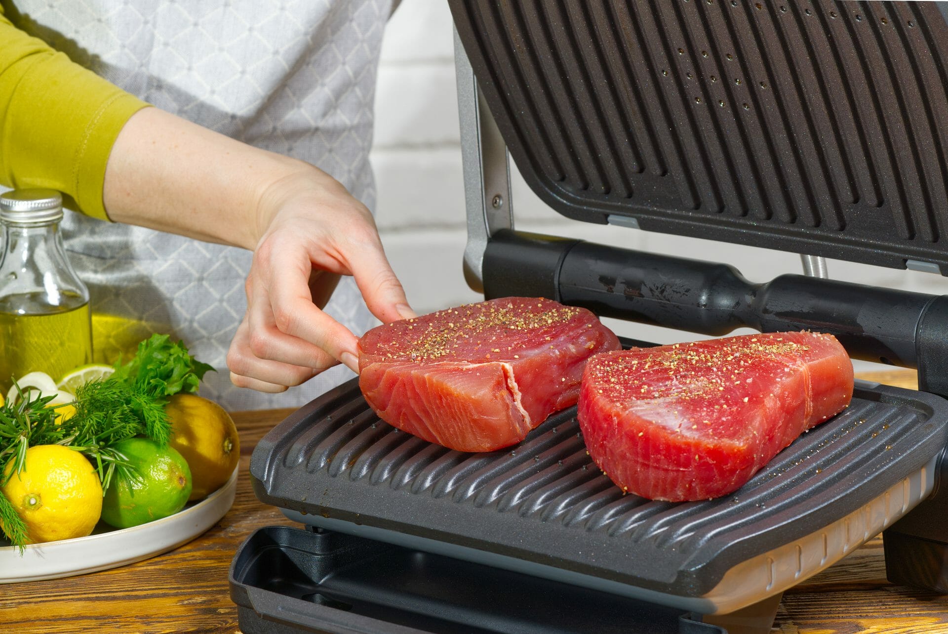 woman's hand putting fish-steak on electric grill 